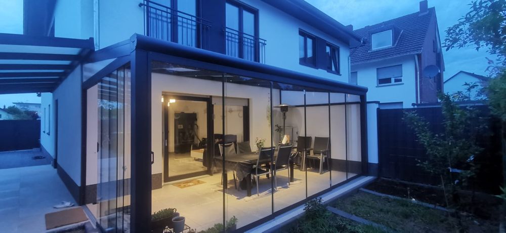 Terrassenüberdachung mit rahmenlosen Glasschiebewänden, beleuchtet