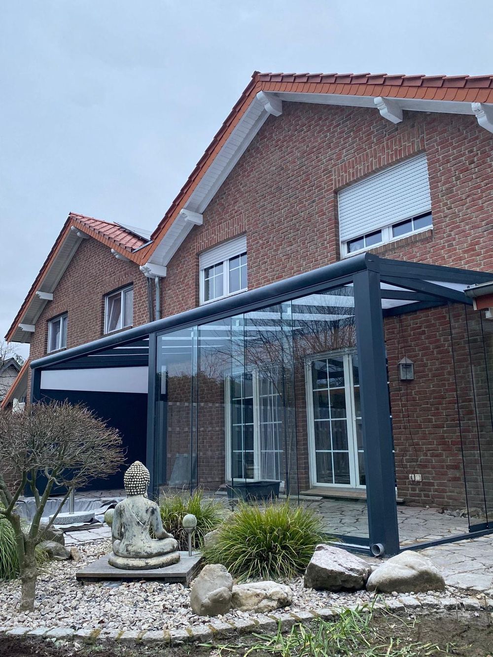Glasschiebewände schützen eine überdachte Terrasse vor Wind