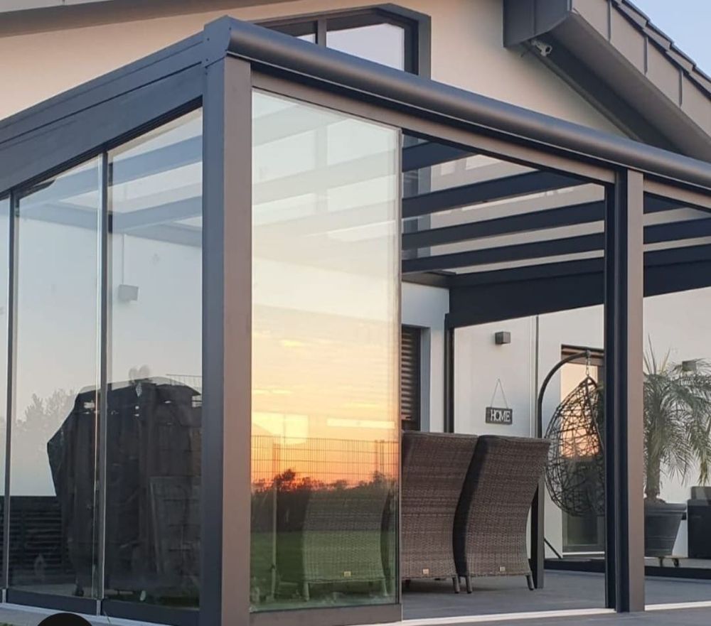 Glasüberdachte Terrasse mit Glasschiebewänden bei Sonnenuntergang