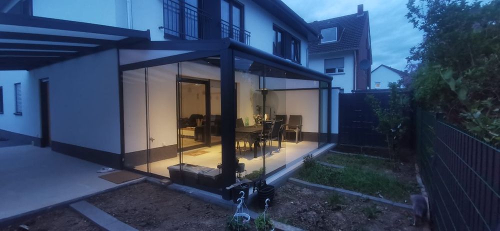 Überdachte Terrasse mit Glasschiebewänden am Abend